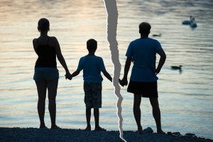 Photo of mother, son and father holding hands, with the photo is ripped in half between the father and son.