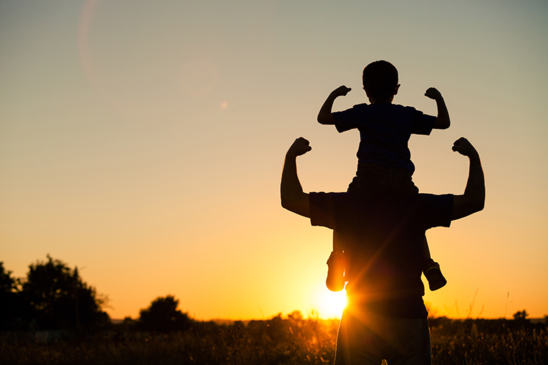 Child sitting on parents shoulders during sunset