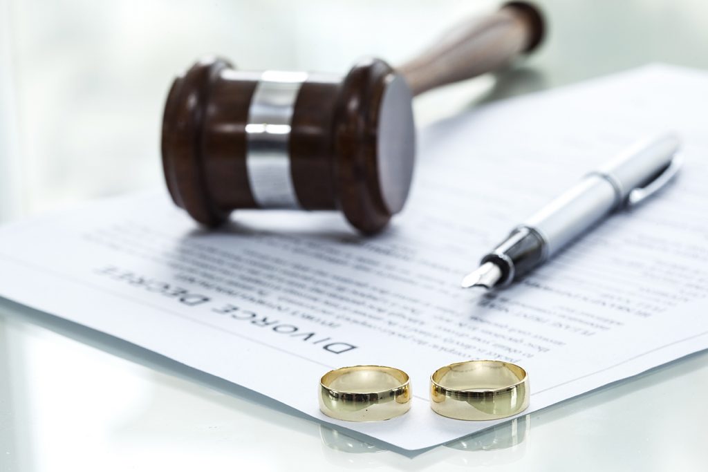 Judges hammer, two gold rings and a pen on top of divorce papers