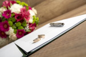 Wedding bands and a pen sitting on paper next to flowers