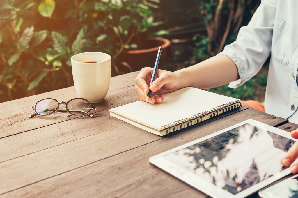 Person working at desk outside writing on a notebook