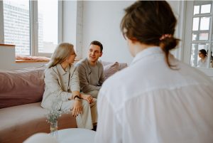 Couple sitting on couch and talking with person in a white shirt