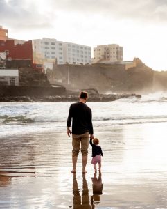 Man and child standing on a beach with city in background