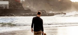 Man and child standing on beach with city in background