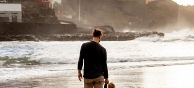 Man and child standing on beach with city in background
