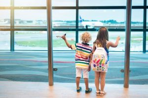 Two children standing in airport watching airplanes through the window