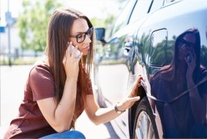 Woman on phone and looking at car damage