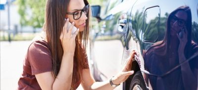 Woman on phone and looking at car damage
