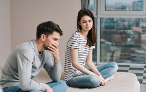 Man and woman sitting on a bed, both are upset