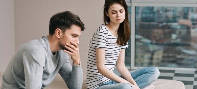 Man and woman sitting on a bed, both are upset