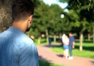 Man standing behind a tree watching a couple